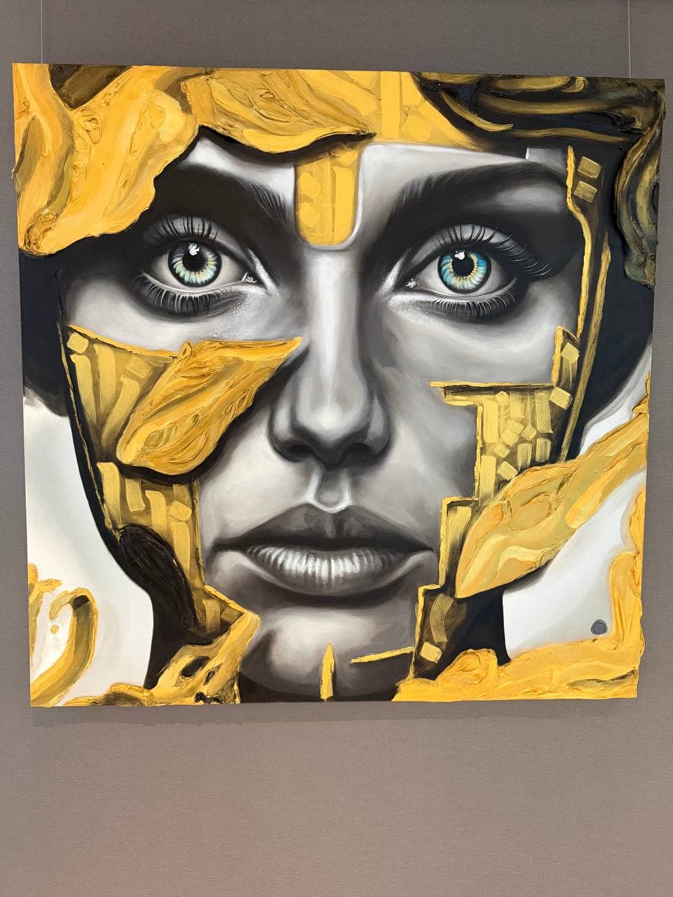 Chronodermism Unlayering by Rudy Hetzer, a square mixed media portrait with a grayscale face, blue-green eyes, black shadow forms, and thick golden textured layers across the surface.