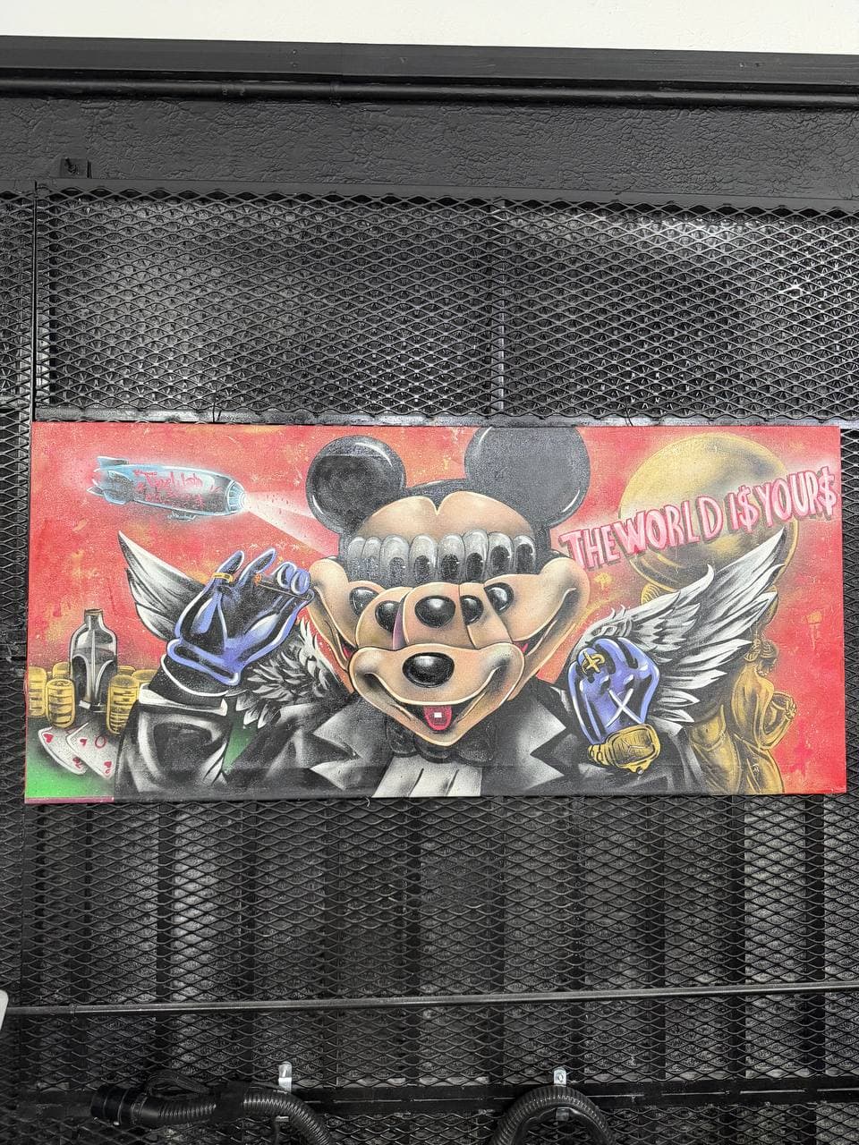 9Juane$ artwork God Mickey showing a winged cartoon-inspired figure with gold coins, a blimp, and The World Is Yours text on a red field.