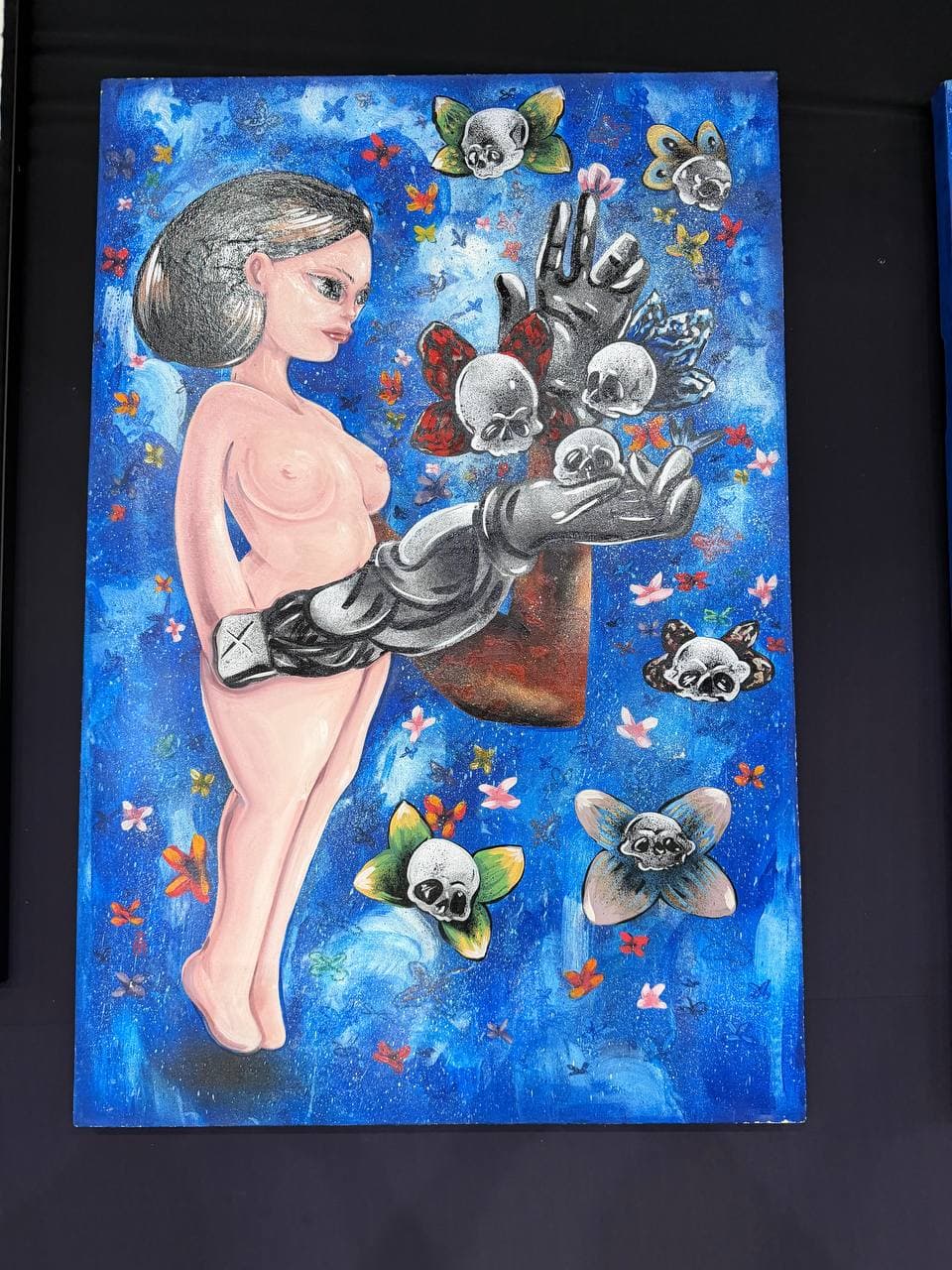 9Juane$ artwork Papillon showing a surreal female figure on an electric-blue field with butterflies, skull forms, and a mechanical arm.